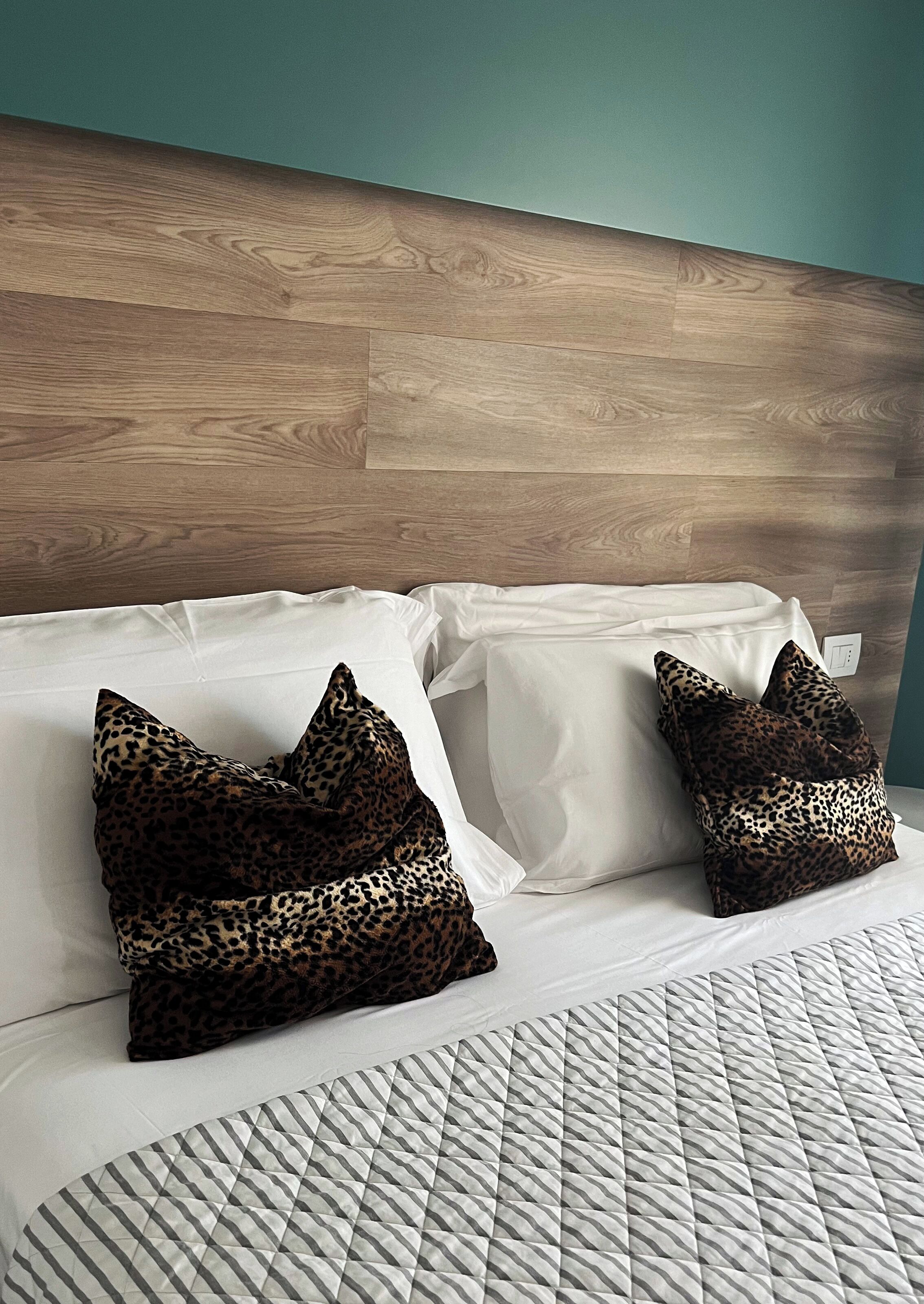 A bed with white linens, two leopard print pillows, and a quilted bedspread.