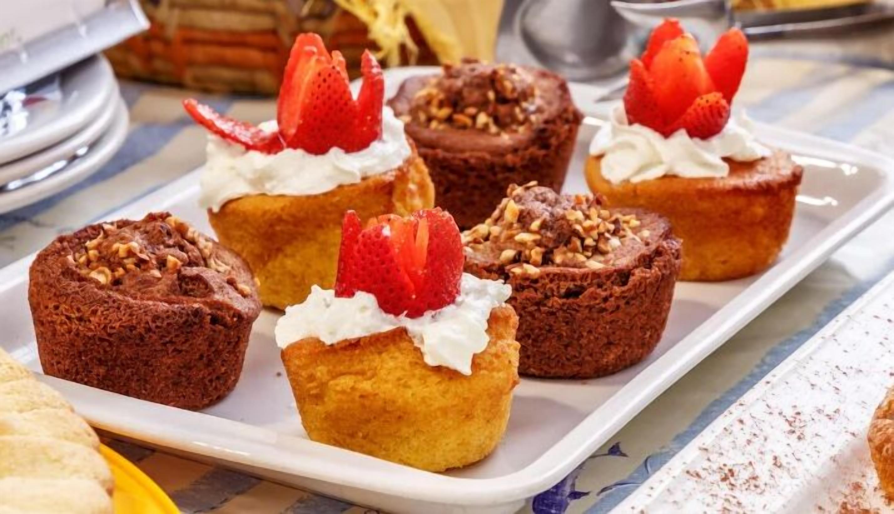 A tray of mini cakes with whipped cream and strawberries.