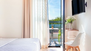Ein Schlafzimmer mit einem Bett, einem Schreibtisch mit Stuhl, einem Fernseher und einem Balkon mit Tisch und Stühlen.