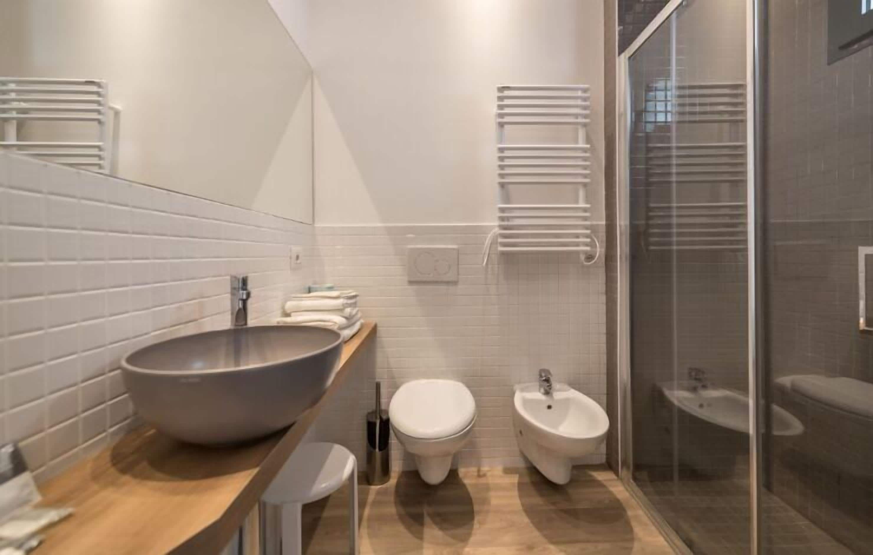 A modern bathroom with a large vessel sink, two toilets, a bidet, and a glass-enclosed shower.