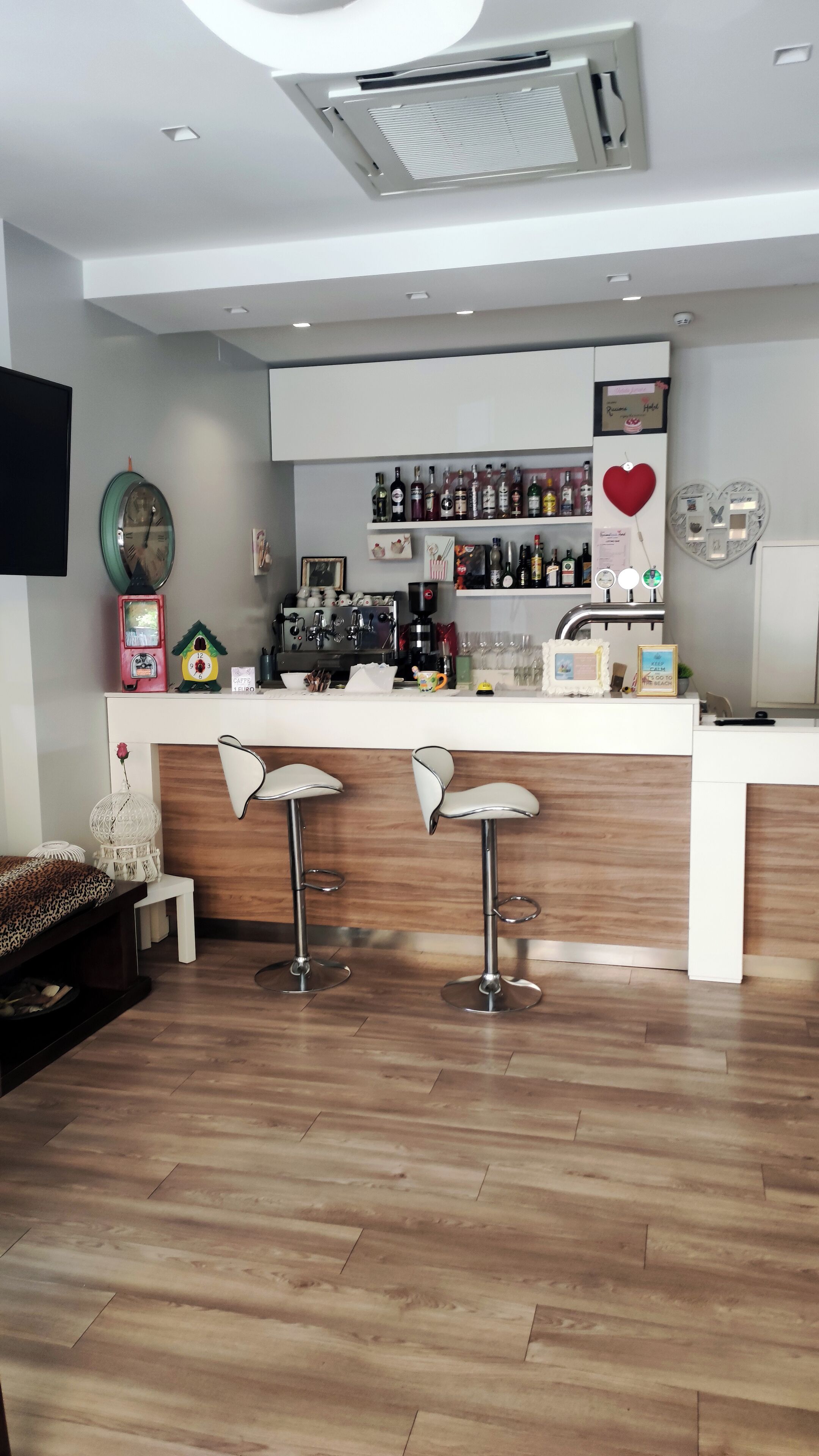 A modern bar area with a wooden counter, two bar stools, and a variety of bottles and glasses on shelves.