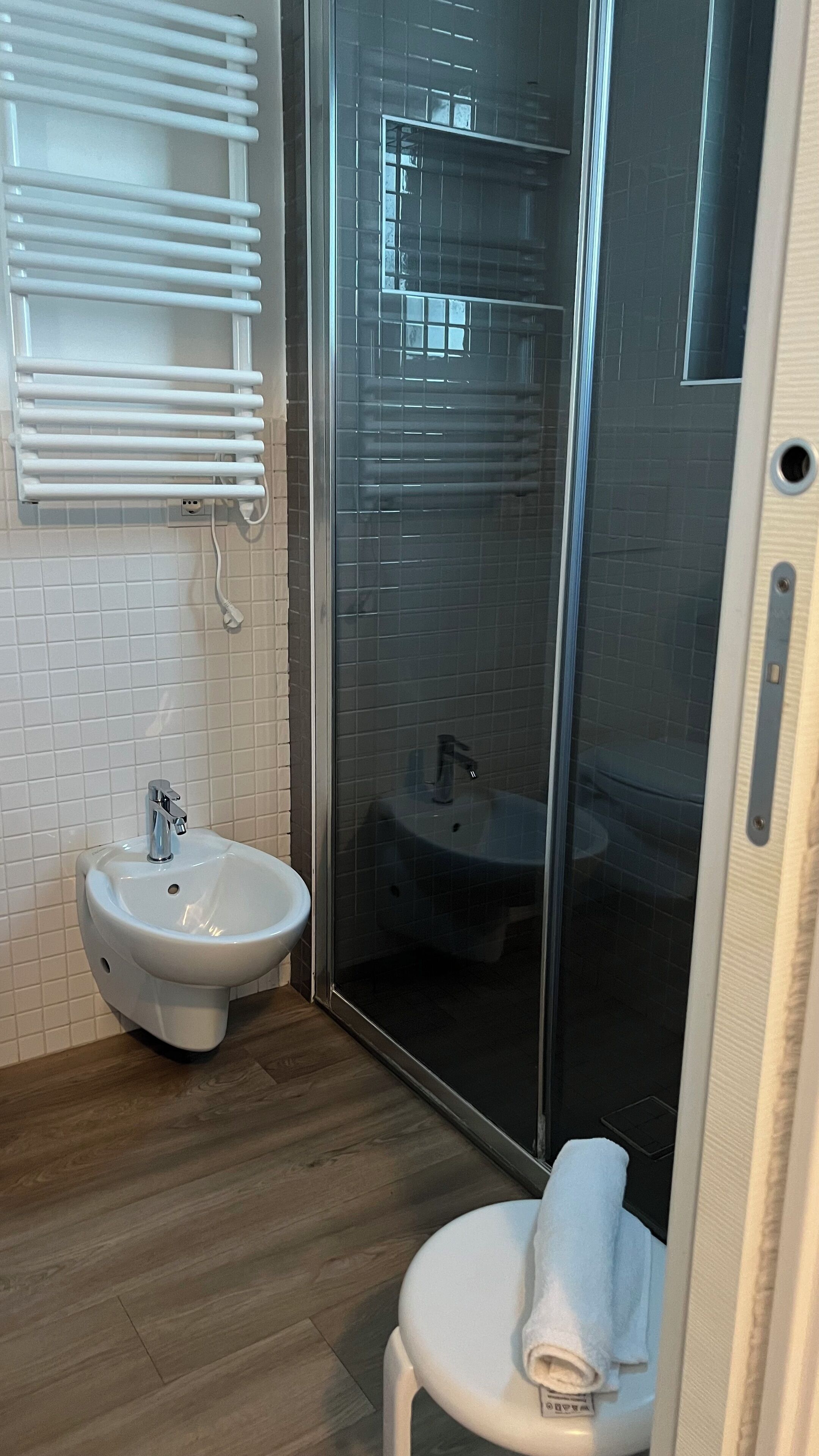 A modern bathroom with a glass shower enclosure, a white sink, and a towel on a chair.