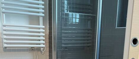 A modern bathroom with a glass shower enclosure, a white sink, and a towel on a chair.