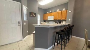 A kitchen with a central island, bar stools, wooden cabinets, and a microwave. - Relaxing 3 Bedroom Townhome (Kissimmee)