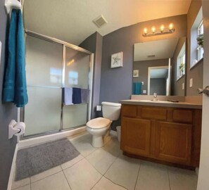 Ein Badezimmer mit Duschkabine aus Glas, Toilette, Holzwaschtisch mit Spiegel und Handtuchhalter.