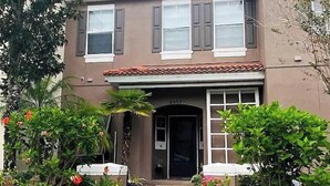 A two-story house with a front entrance, a covered porch, and a small garden with various plants and flowers. - Relaxing 3 Bedroom Townhome (Kissimmee)