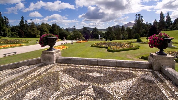 A garden with a patterned stone floor, flower beds, and a view of a mountainous landscape. - Aughrim Holiday Village No 14 (Aughrim)