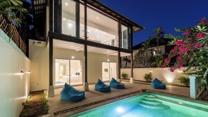 Una casa moderna de dos pisos con piscina, puertas de vidrio que dan a un dormitorio y pufs azules.