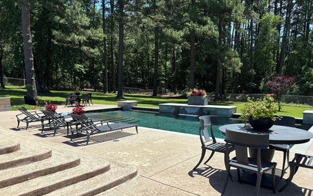 A swimming pool with a waterfall feature, surrounded by outdoor seating and a stone staircase.