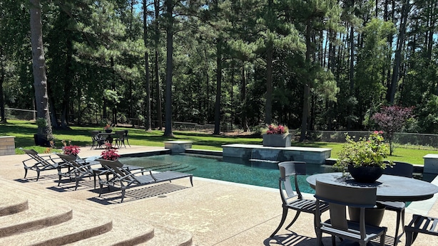 A swimming pool with a waterfall feature, surrounded by outdoor seating and a stone staircase. - Perfect Poolhouse (Linden)