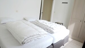 Ein ordentlich bezogenes Bett mit weißen Laken in einem Zimmer mit Tür und Kleiderschrank.