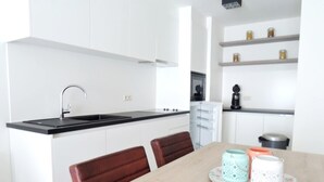 Eine moderne Küche mit weißen Schränken, einer schwarzen Arbeitsplatte und einem Essbereich mit Holztisch und Stühlen.