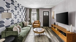 Una sala de estar moderna con un sofá verde, una mesa de centro de madera, un sillón de cuero y un televisor de pantalla plana montado en la pared.