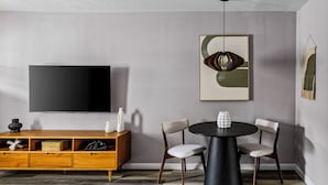 Una sala de estar moderna con un televisor de pantalla plana, una mesa de comedor redonda, dos sillas, un aparador de madera y arte abstracto en la pared.
