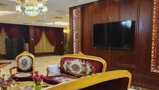 Ein luxuriöses Zimmer mit aufwendigen Möbeln, einer Kristallleuchtre und einem großen Flachbildfernseher, der an einem Holzpaneel befestigt ist.