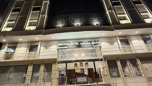 Ein Hotel mit einem großen Rundbogen-Eingang, mehreren Balkonen mit aufwendigen Geländern und einem Schild, das es als Meezab Hotel in Al Rawdah kennzeichnet.