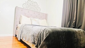 A bedroom with a tufted headboard, a bed with a grey blanket, and a wooden floor. - Cozy 2BER 1.5 Bath Home Near Rogers/2min walk 2 Stadium/RAH /NAIT/FastWIFI/Parkx (Edmonton)