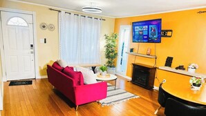 A living room with a red sofa, a coffee table, a TV mounted on the wall, and a fireplace. - Cozy 2BER 1.5 Bath Home Near Rogers/2min walk 2 Stadium/RAH /NAIT/FastWIFI/Parkx (Edmonton)