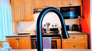 A kitchen with wooden cabinets, a stainless steel sink, a black faucet, a stove, and a microwave. - Cozy 2BER 1.5 Bath Home Near Rogers/2min walk 2 Stadium/RAH /NAIT/FastWIFI/Parkx (Edmonton)