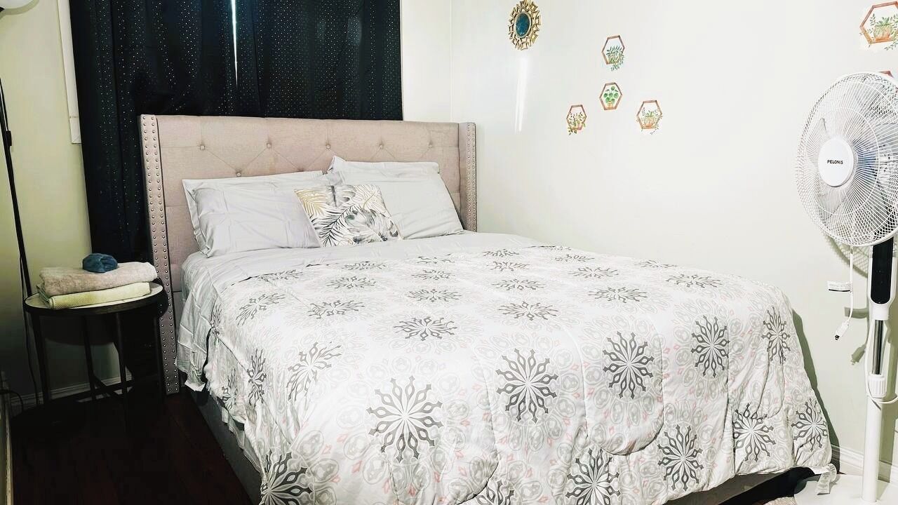 Un dormitorio con cama, mesita de noche, ventilador y decoración en la pared.