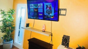 A living room with a flat-screen TV mounted on the wall displaying various streaming channels. - Cozy 2BER 1.5 Bath Home Near Rogers/2min walk 2 Stadium/RAH /NAIT/FastWIFI/Parkx (Edmonton)