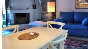 Ein gemütlicher Raum mit Steinwand, Kamin, blauem Sofa und Esstisch mit Stühlen.