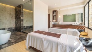 Moderni hotellihuone, jossa on suuri kylpyamme, kaksi valkoisilla lakanoilla varustettua sänkyä, suuri peili ja näkymä kaupunkiin.