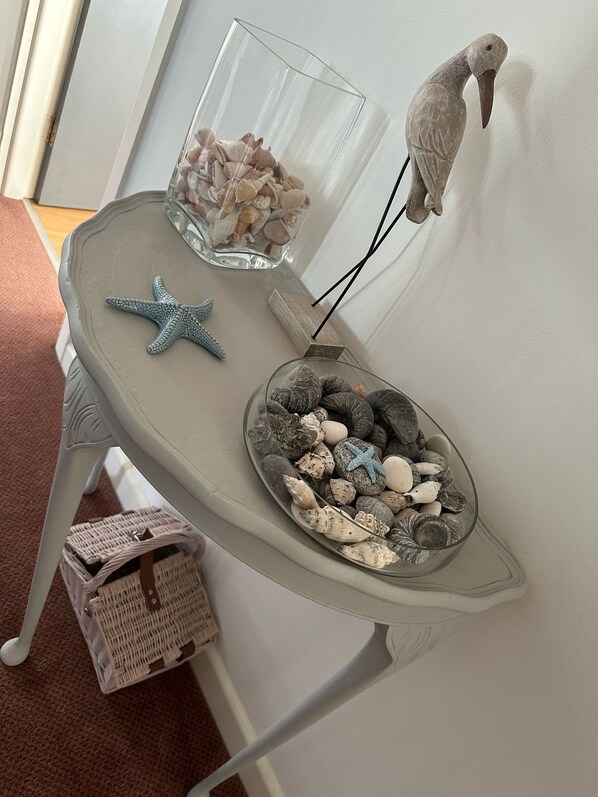 A small table with a glass bowl of seashells, a starfish, and a decorative bird on a wall.