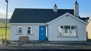 Ein kleines, eingeschossiges Haus mit einer blauen Tür und einer Bank vor der Tür, bewölkter Himmel.