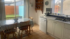 Eine Küche mit Esstisch, Stühlen, Geschirrspüler und einem Fenster mit Blick auf einen Garten.