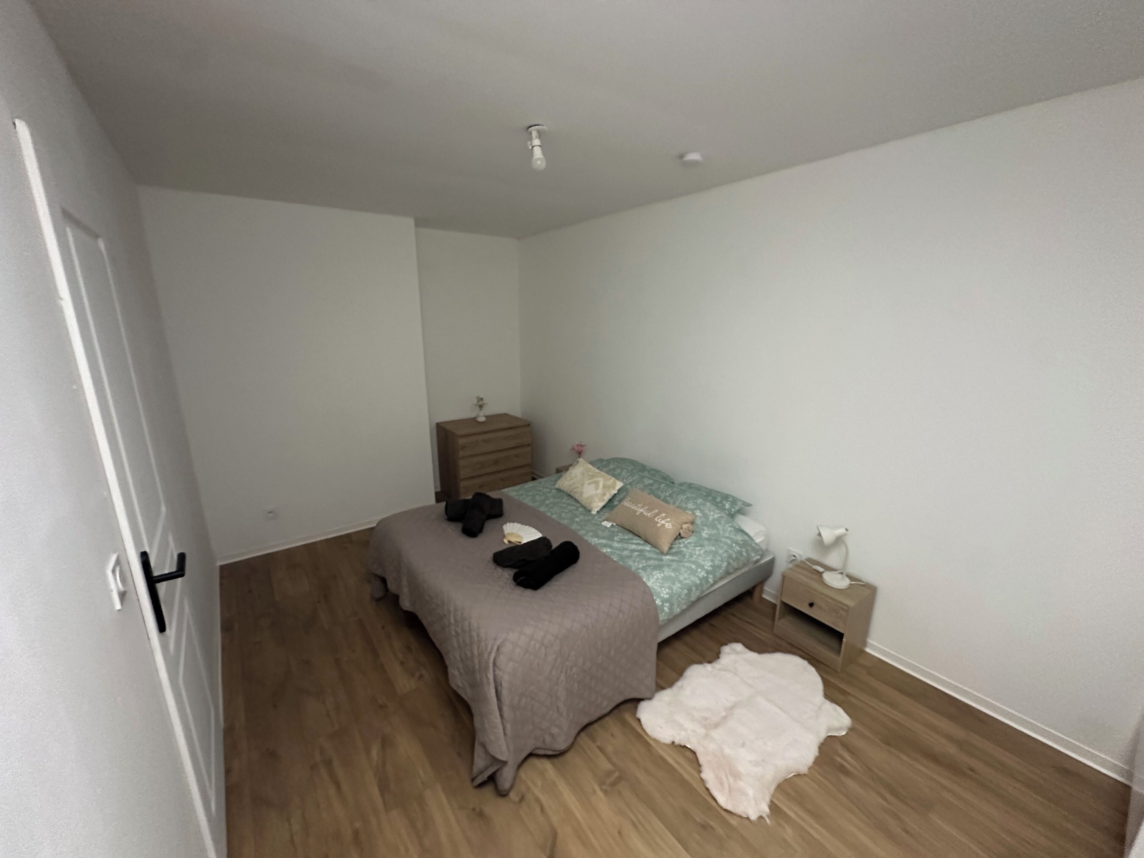 Une chambre à coucher comprenant un lit, une table de chevet, une commode, une porte et un luminaire.