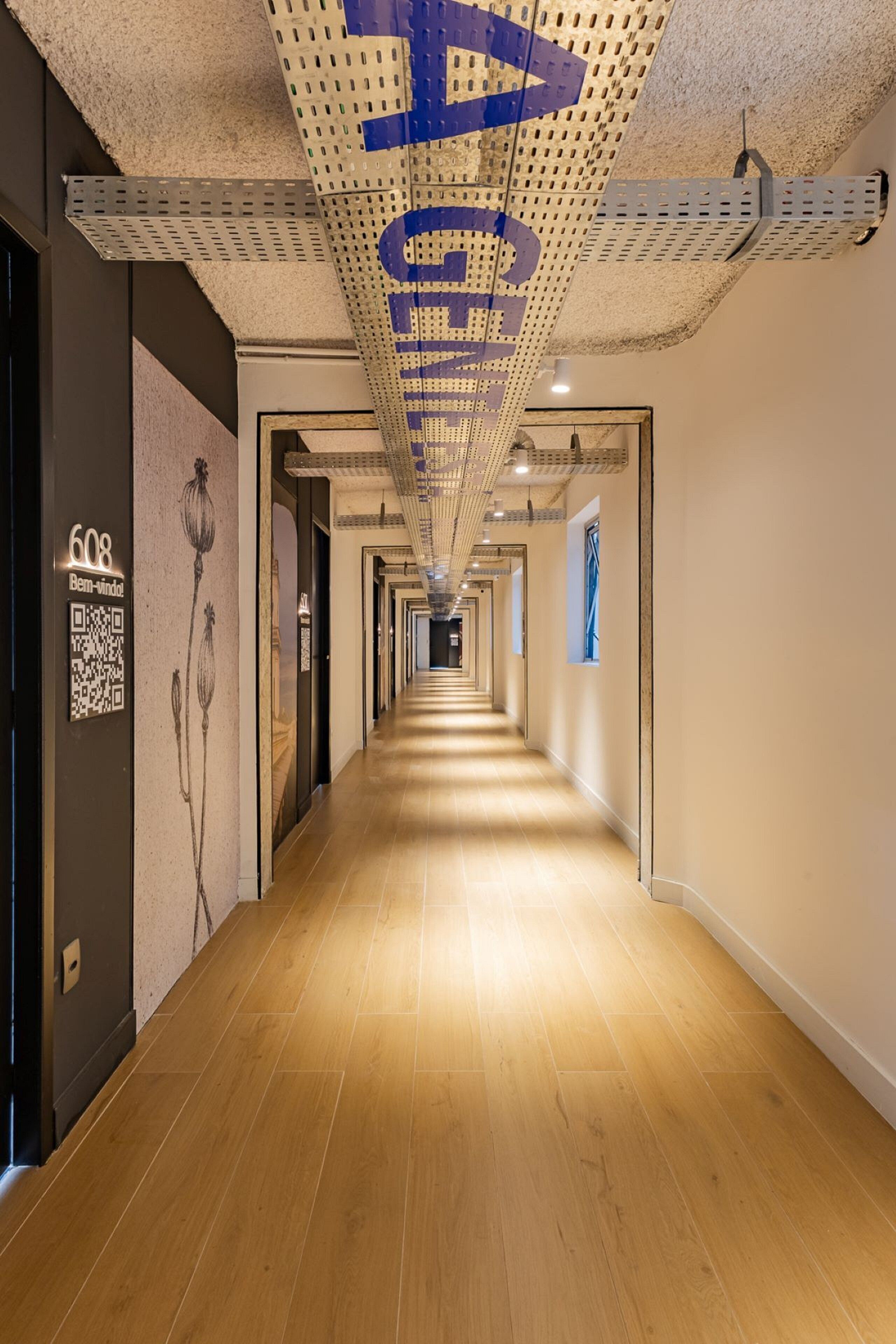 A hotel corridor with a wooden floor, a QR code, and a number sign.
