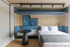 Une chambre à coucher moderne avec un lit, un canapé, une table ronde et des œuvres d’art abstraites accrochées au mur.