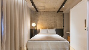 A modern bedroom with a large bed, a headboard, a bedside table with a lamp, and a wardrobe.