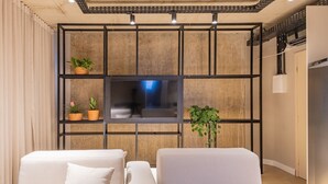 A modern living room with a flat-screen TV mounted on a wooden panel wall, two sofas, and potted plants.