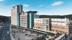 A multi-story building with a mix of modern and traditional architecture, a parking lot, and a road with vehicles.