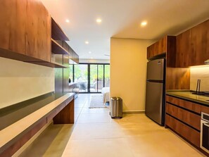 A modern kitchen with wooden cabinets, a stainless steel refrigerator, and a large window providing natural light.