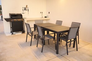 A kitchen area with a grill, a dining table with chairs, and a countertop with a sink and utensils.