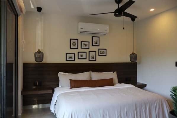 Ein modernes Schlafzimmer mit einem großen Bett, einem Deckenventilator, einer Klimaanlage und gerahmten Bildern an der Wand.