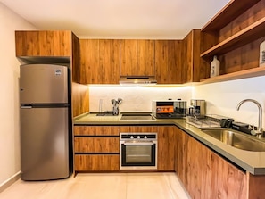 A compact kitchen with wooden cabinets, a stainless steel refrigerator, a built-in oven, and a sink.