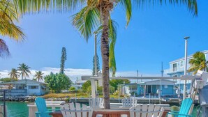 A poolside area with white Adirondack chairs, a wooden table, and a palm tree. - On Island Time! HotTub-Water View (Marathon)