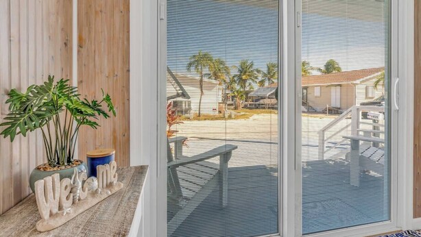 A sliding glass door leading to a balcony with a view of a residential area, a welcome mat, and a potted plant. - On Island Time! HotTub-Water View (Marathon)