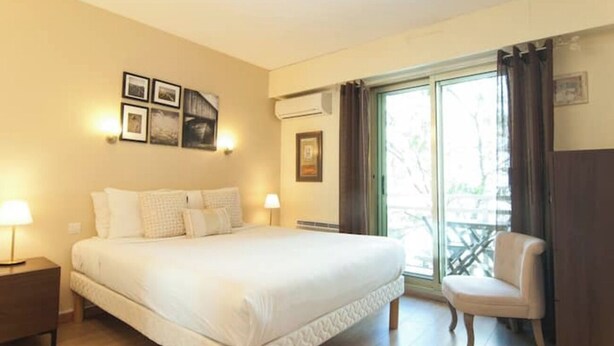 A bedroom with a large bed, two bedside lamps, a chair, and a window with curtains. - Elegant Apt w/2 Terraces/Mins to Beach & Shops (Antibes)
