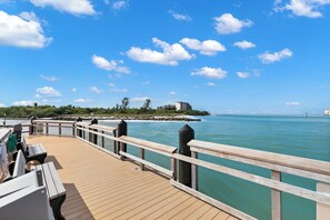 Eine Holzstege mit Bänken, einer Geländer und Blick auf das Meer und entfernte Gebäude.