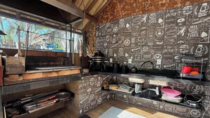 A kitchen with a brick oven, wooden shelves, and a wall decorated with food-related illustrations. - Barra do Sahy 1 (Sao Sebastiao)