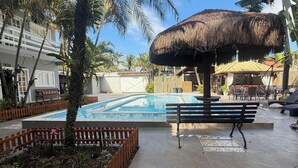 A pool area with a thatched umbrella, wooden benches, and a fenced garden. - Barra do Sahy 1 (Sao Sebastiao)