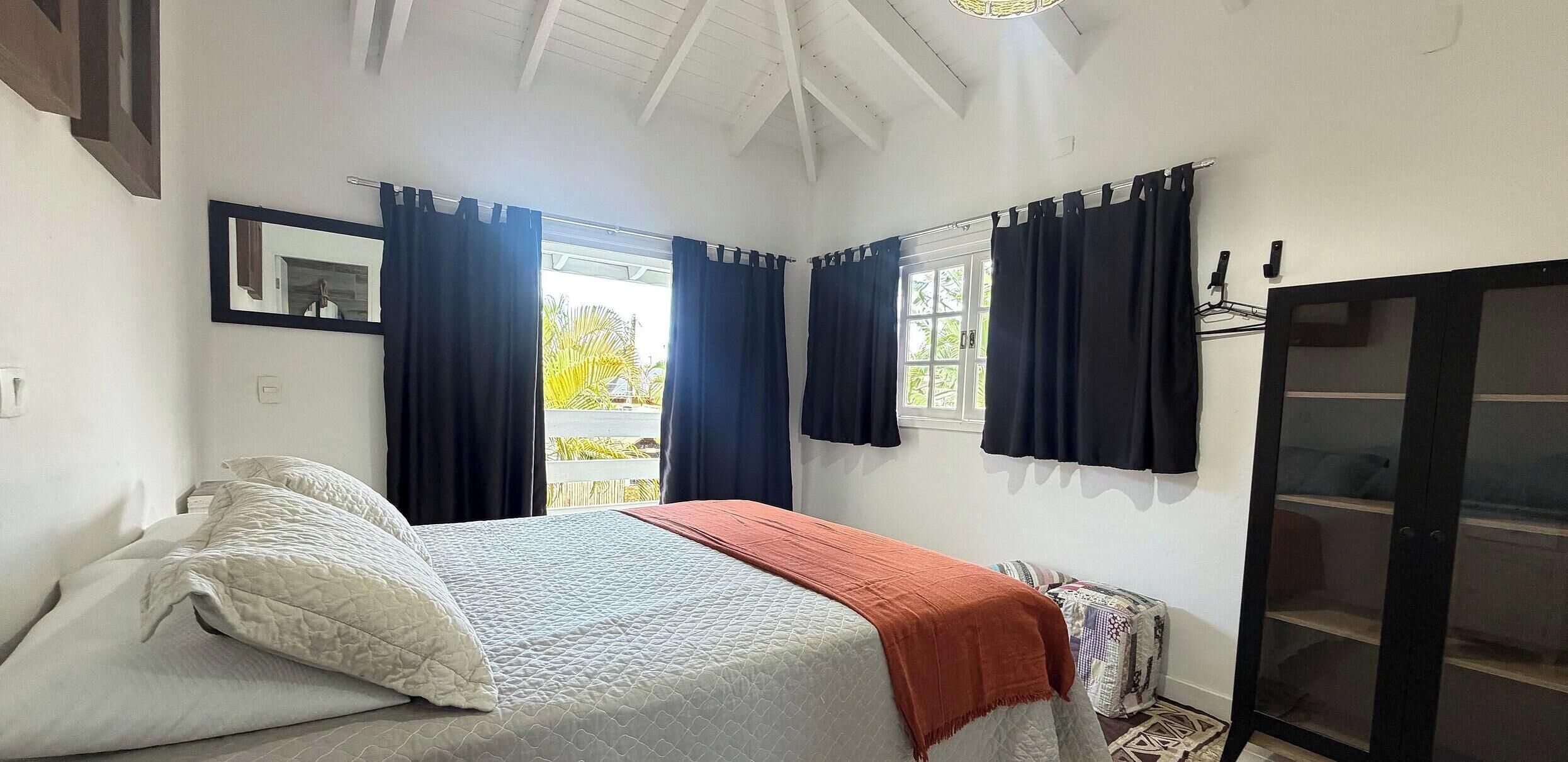 A bedroom with a bed, a window with curtains, a wardrobe, and a ceiling fan.