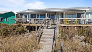 A building with a wooden deck and stairs leading to a covered area with windows. - Just For The Halibut 
Ocean Front Stay
Pet-Friendly (Emerald Isle)
