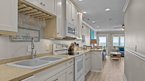 A modern kitchen with white cabinetry, a double sink, and a stove. There is a view of the ocean through large windows. - Just For The Halibut 
Ocean Front Stay
Pet-Friendly (Emerald Isle)