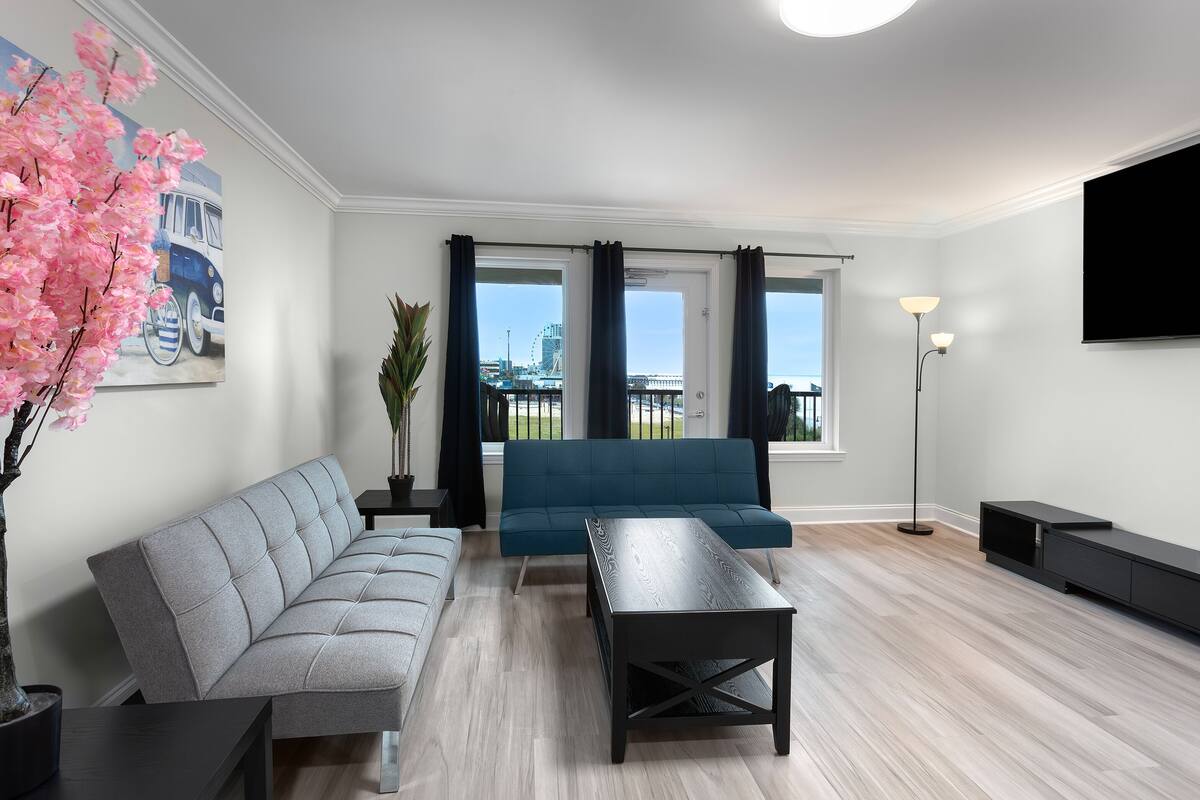 A modern living room with a grey sofa, a matching armchair, a wooden coffee table, and a large window with curtains.